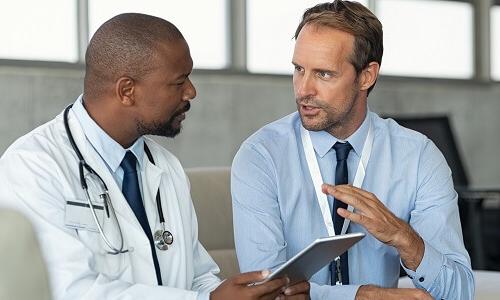 Healthcare administrator and physician discussing data on a tablet in a professional environment, focusing on healthcare management and decision-making.